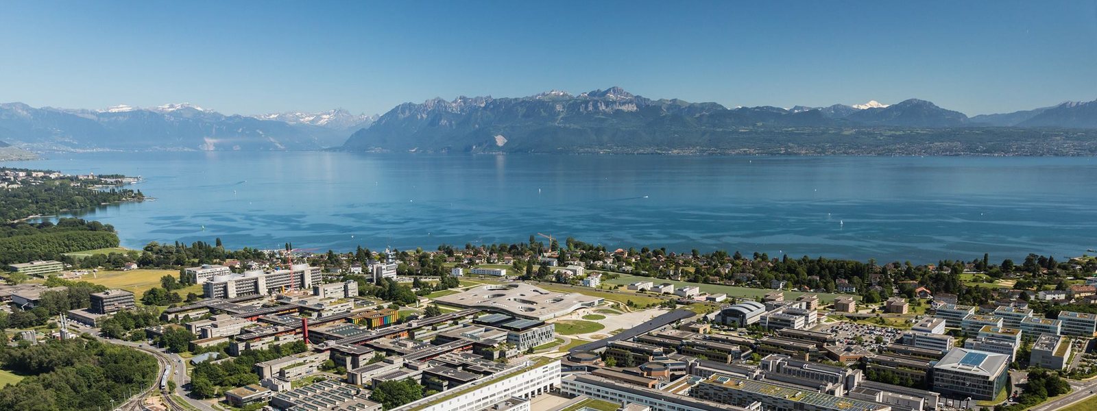 Vue aérienne du campus de l'EPFL au bord du Léman, avec les Alpes en arrière-plan