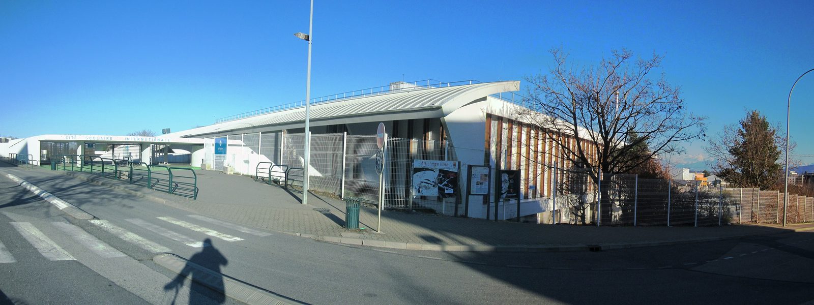 The entrance of the international school complex in Ferney-Voltaire, a long white building with a curved roof under a clear winter sky